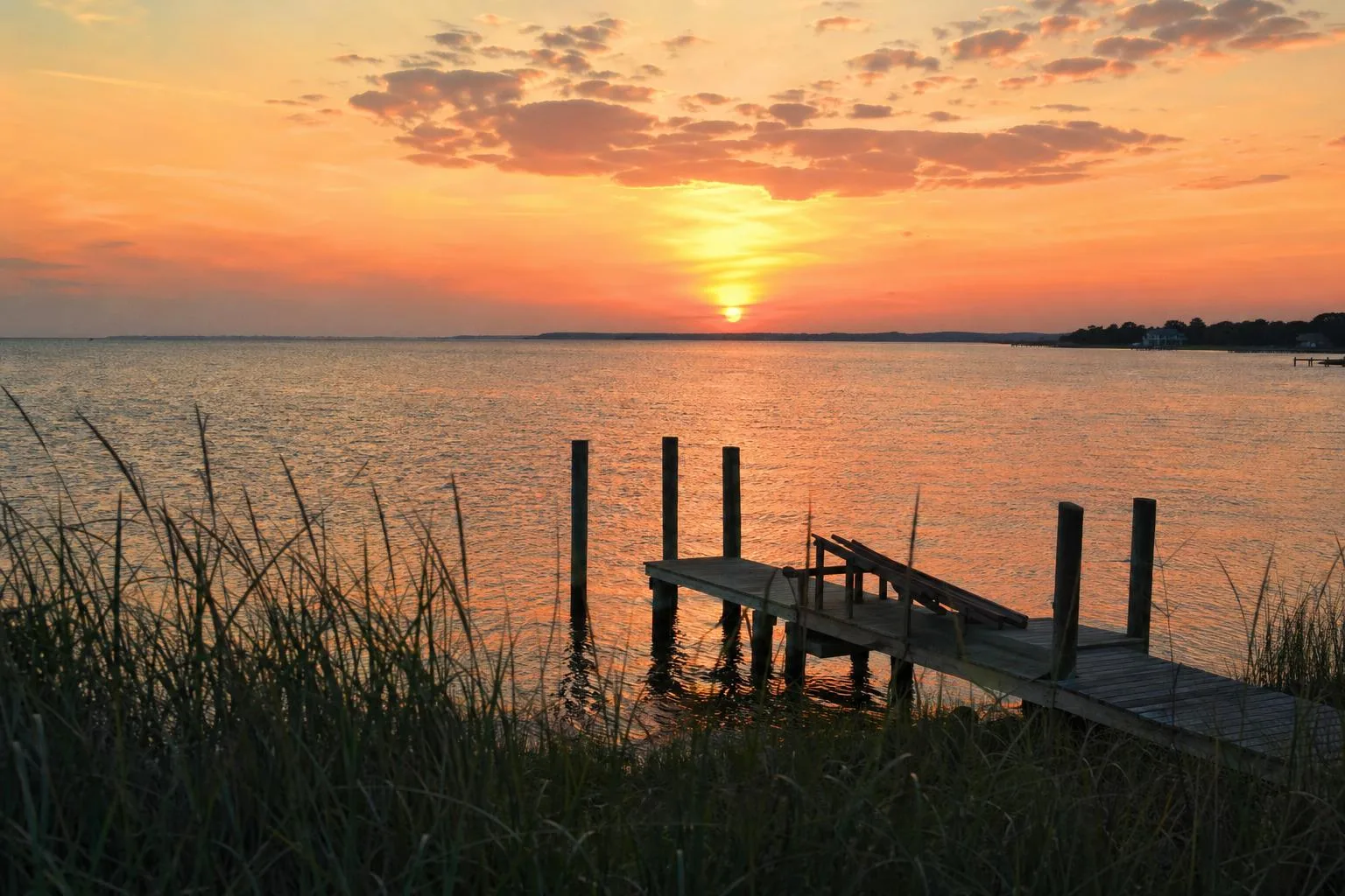 Golden sunset over the Pamlico Sound in Avon NC with a wooden dock and sea grass in the foreground